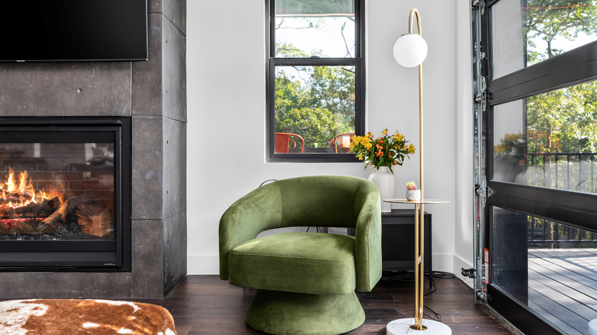 green velvet chair with freestanding lamp next to fireplace and garage door to back patio deck