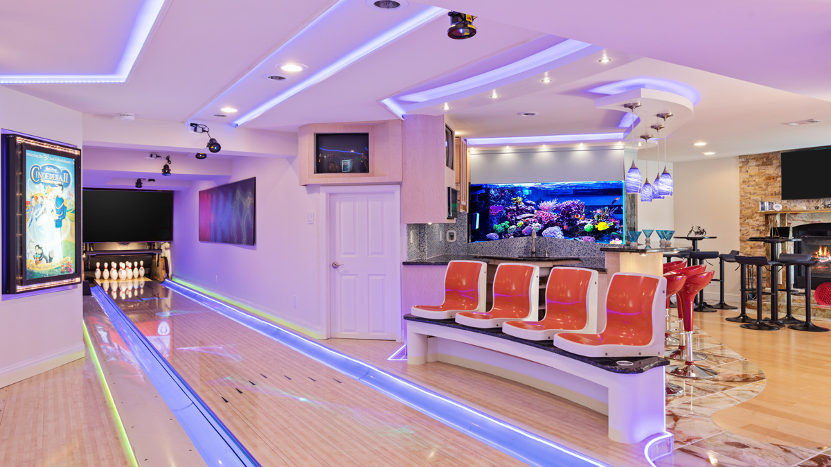 residential basement bowling alley lane with neon lights, seating areas, and tropical aquarium