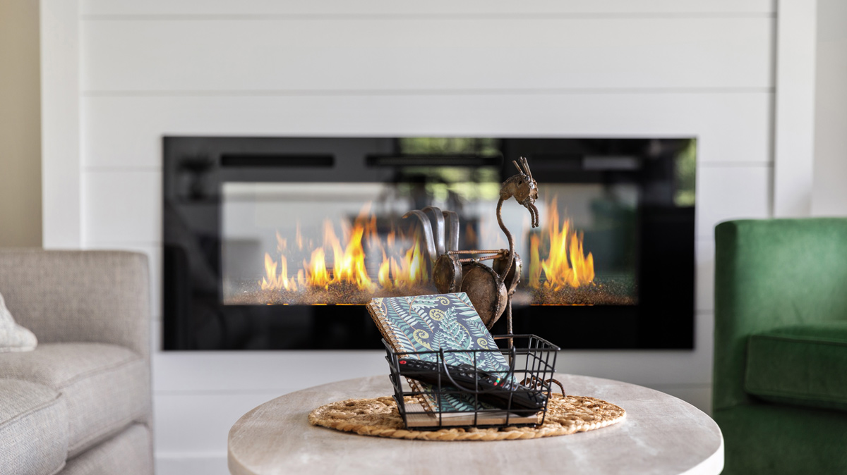 coffee table with wire basket holding a fern covered notebook and tv remotes in front of the electric fireplace