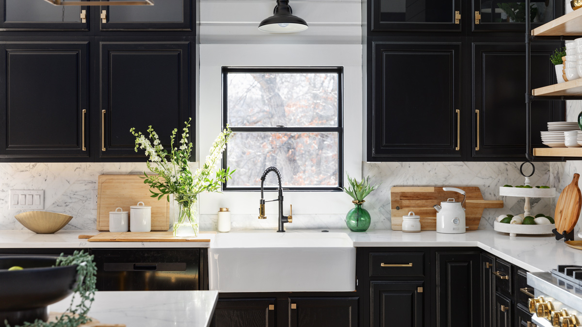 bright kitchen with sink below the window, white counter tops and black cupboards
