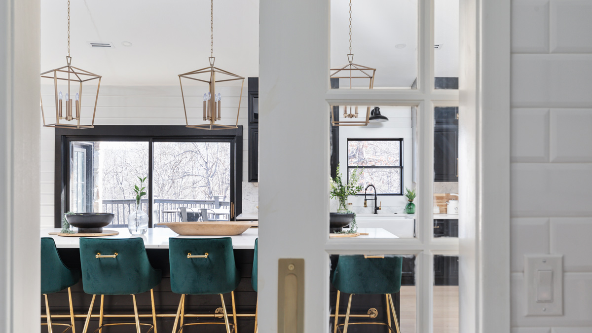 black and white kitchen with open shelving, gas range, and large island with green velvet stools