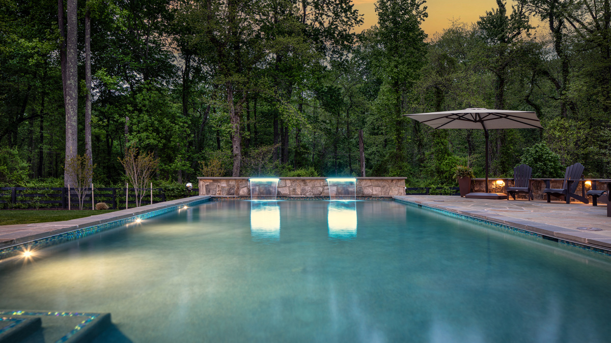 In-ground pool with two waterfalls lit up at dusk