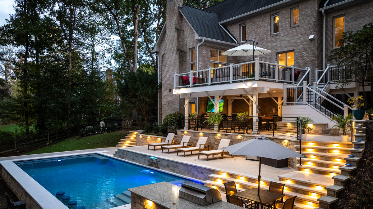 view of the in-ground pool and back patio landscaping lit up at dusk