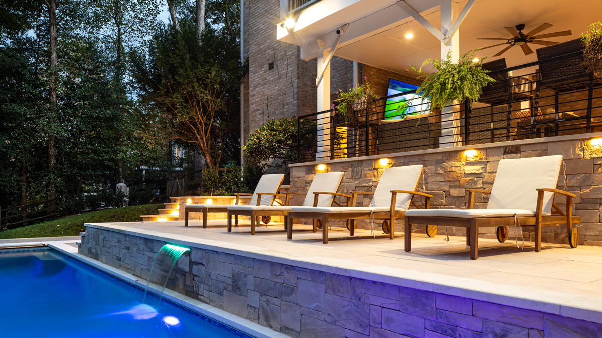 sunbathing lounge chairs lined up between the in-ground pool and patio